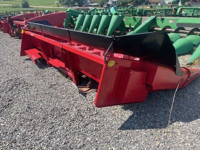 Red farm header attachment with green cones, parked on gravel lot outdoors