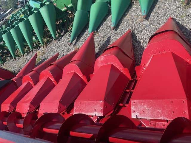 Rows of red and green metal cone-shaped buoys stacked outdoors on gravel.