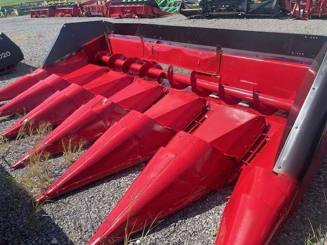 Red combine corn header with pointed harvesting cones on gravel, shown in close-up.