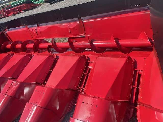 Red metal industrial chute or hopper with bolted seams and a black pipe running across the top