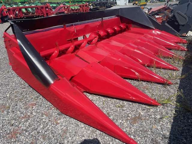 Red agricultural corn header with red pointed snouts on gravel lot