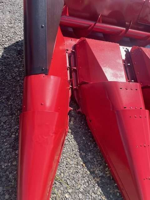 Close-up of red metal farm machinery parts with a black vertical support on gravel.