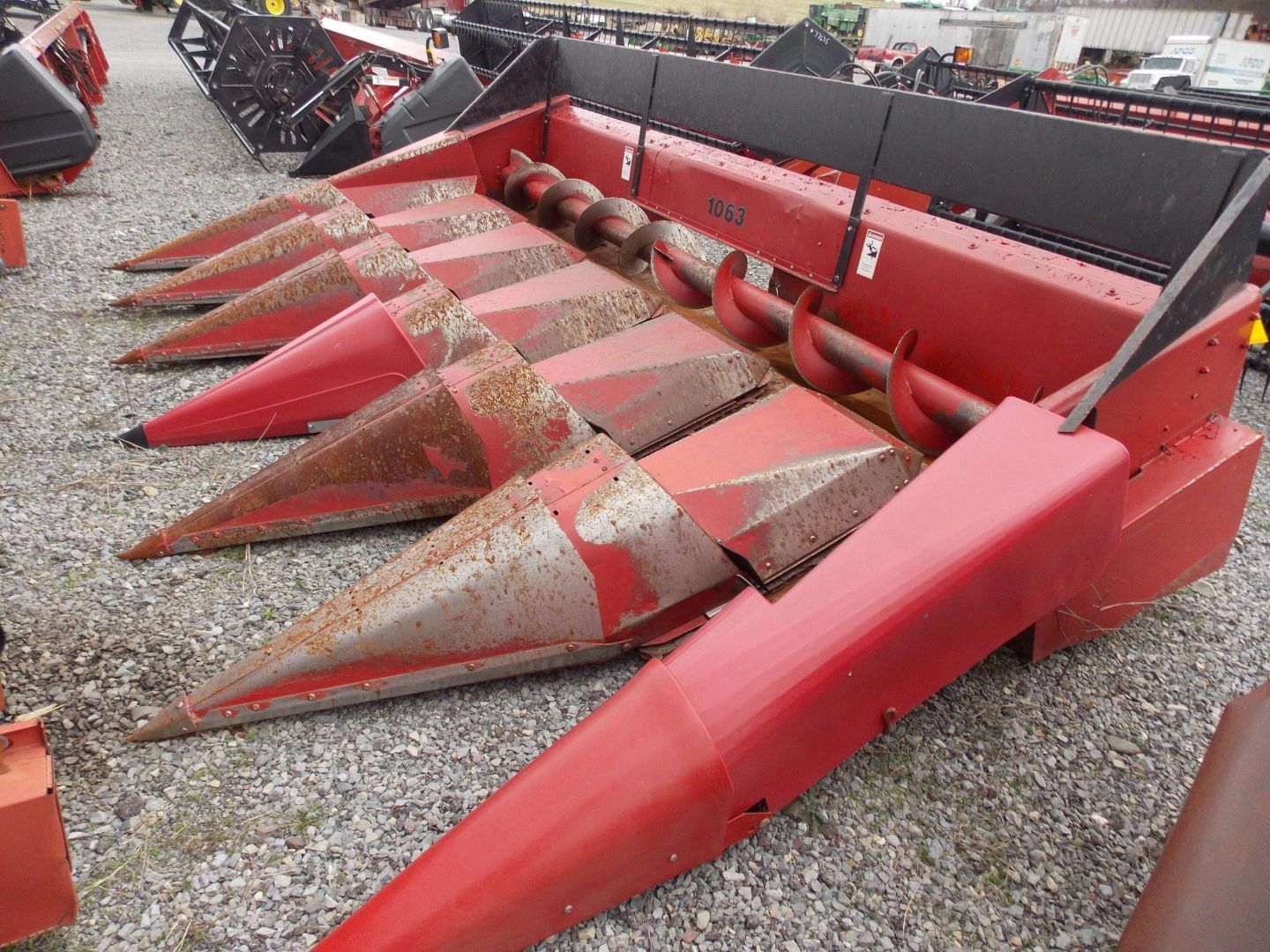 Red agricultural header with pointed red cones and a black frame sitting on gravel.