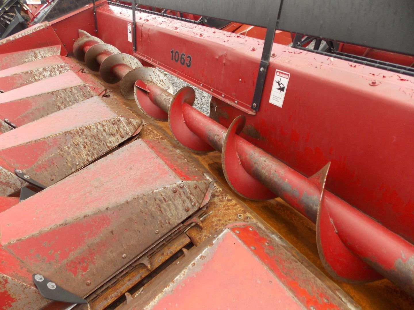 Red agricultural header with red augers and metal dividers, shown close up indoors