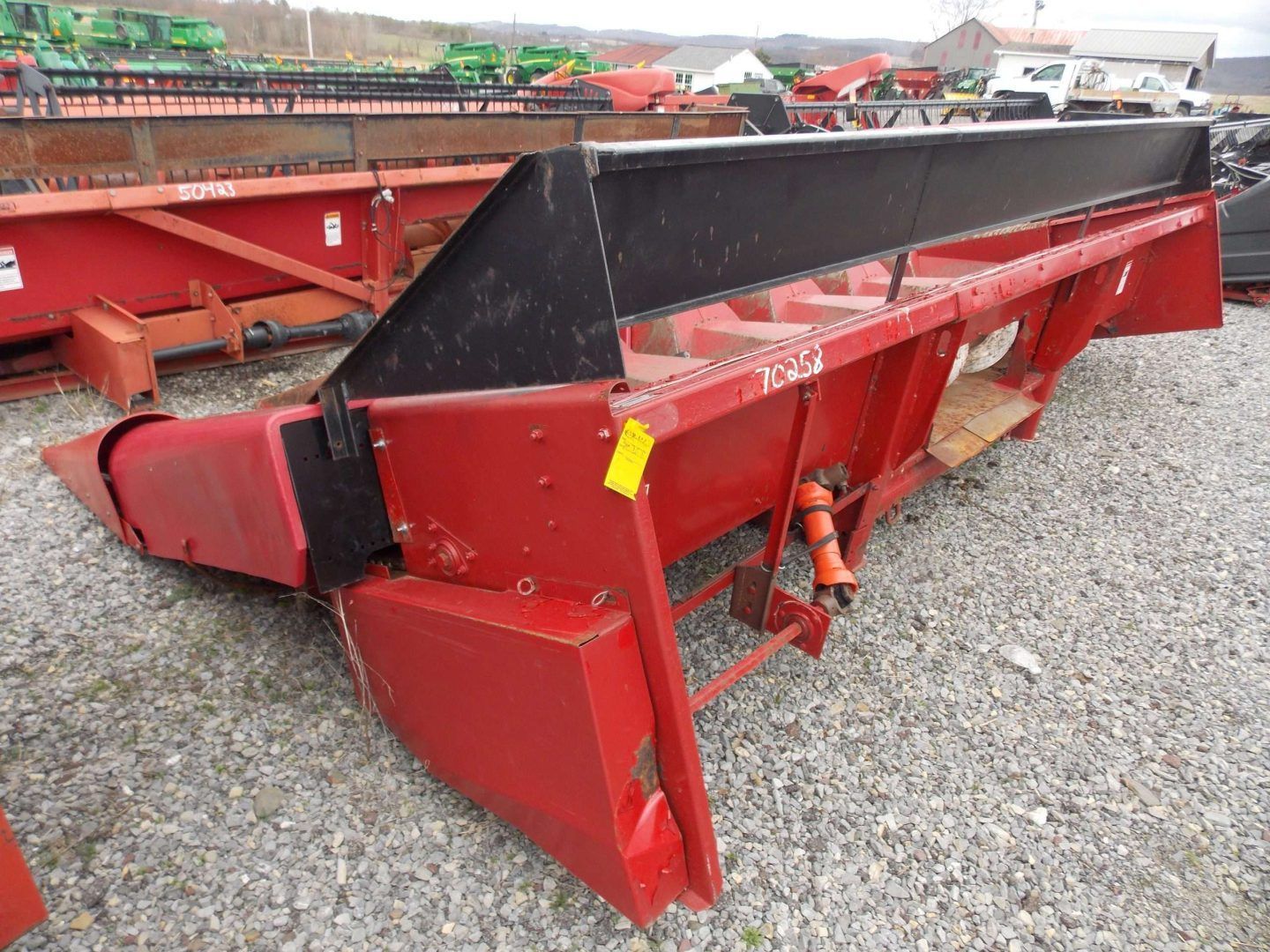 Red agricultural combine header on gravel lot, painted red and black.