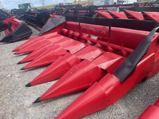Red farm combine corn header with pointed red and black metal rows on gravel lot
