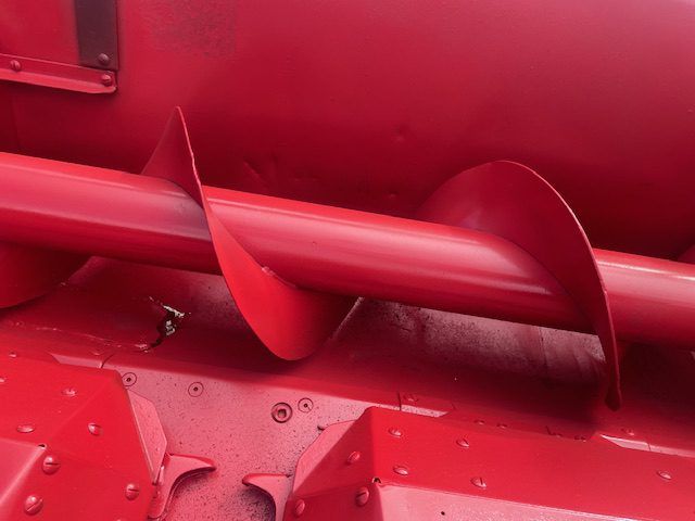 Close-up of a red metal auger screw inside industrial machinery