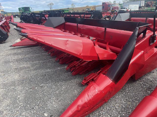 Row of red farm corn headers parked outdoors on a gravel lot