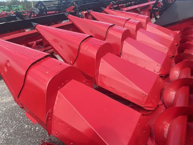 Red agricultural harvesting machine with bright red metal blades and parts stacked outdoors