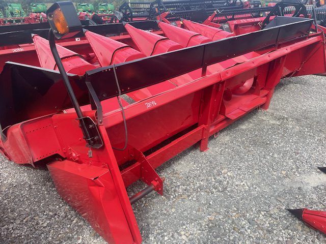 Red agricultural harvesting machine with a wide red conveyor, shown parked on gravel outdoors
