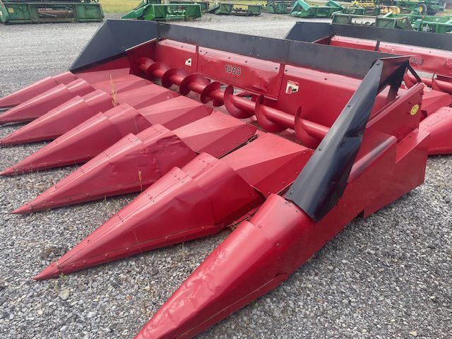 Red agricultural corn header with pointed red cones and black side panels on gravel surface