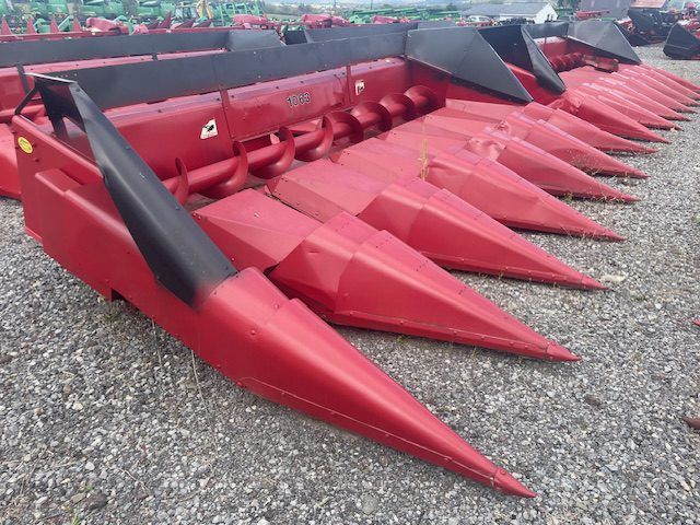 Red corn harvester header with pointed red cutting snouts on gravel