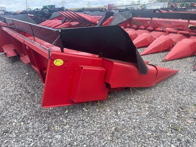 Rows of red agricultural harvesting attachments stacked on gravel outdoors