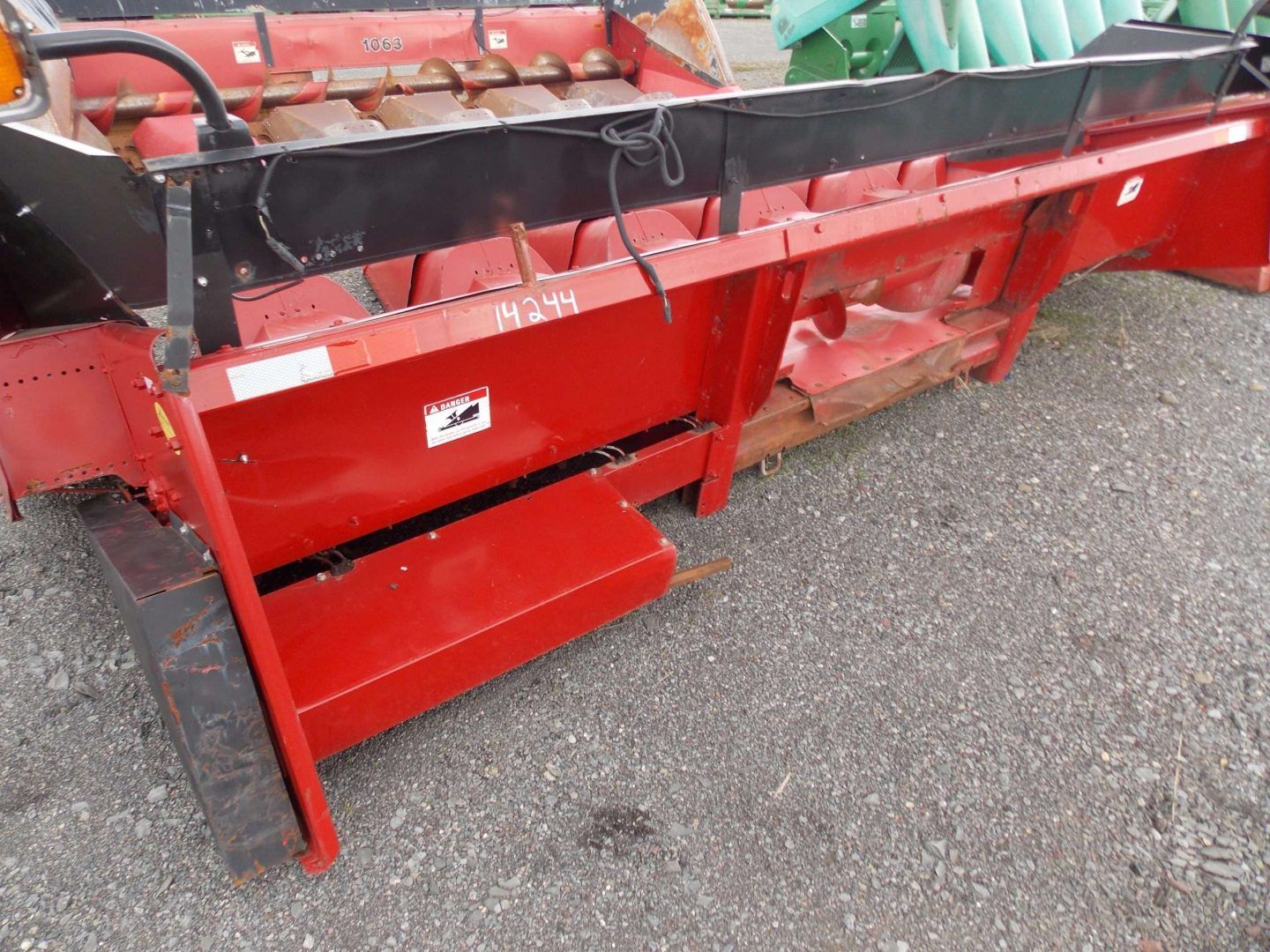 Red agricultural machine attachment with a metal guard and red panels on gravel