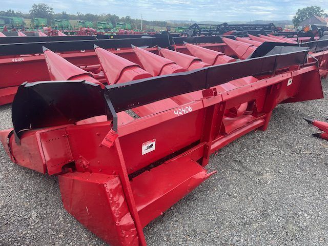 Red farm combine header attachment on gravel lot, with red auger and black end cap.