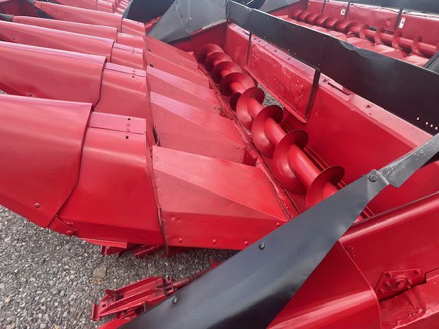 Red agricultural machine with damaged red metal panels and exposed internal rollers on gravel.