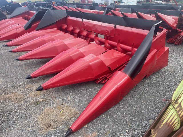 Red industrial harvesting attachments with pointed cones and black tips lined up outdoors on gravel.