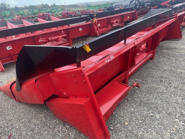 Red agricultural harvesting attachments lined up on gravel outdoors