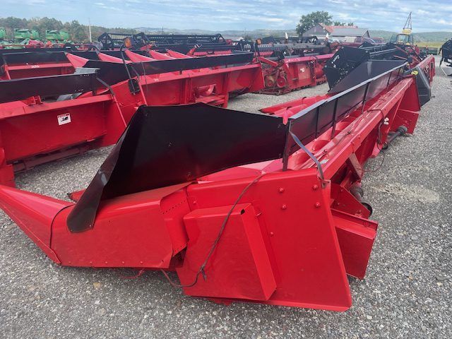 Red agricultural harvesting attachments lined up outdoors in a gravel lot under a cloudy sky
