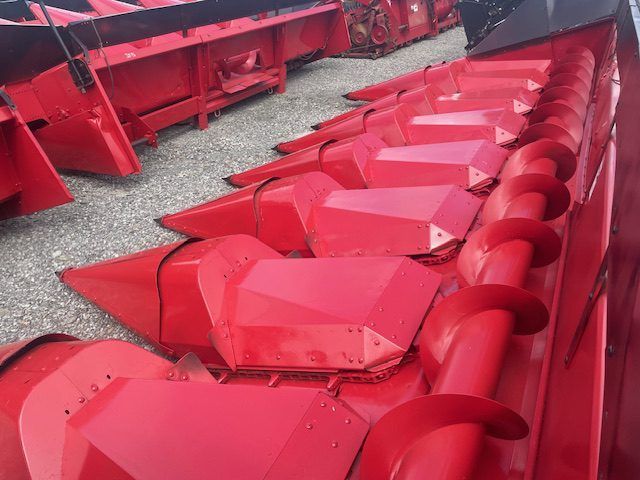 Red agricultural combine header with pink-red metal blades in a gravel yard