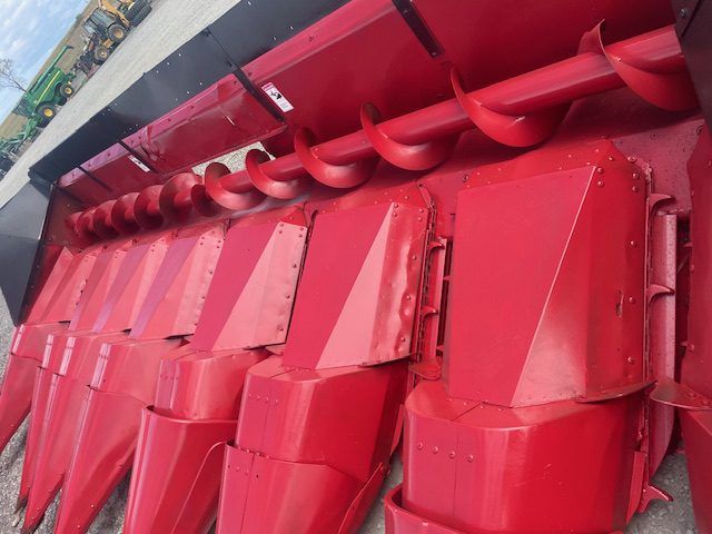 Red agricultural harvester header with multiple metal cutting teeth and red panels, viewed close-up.