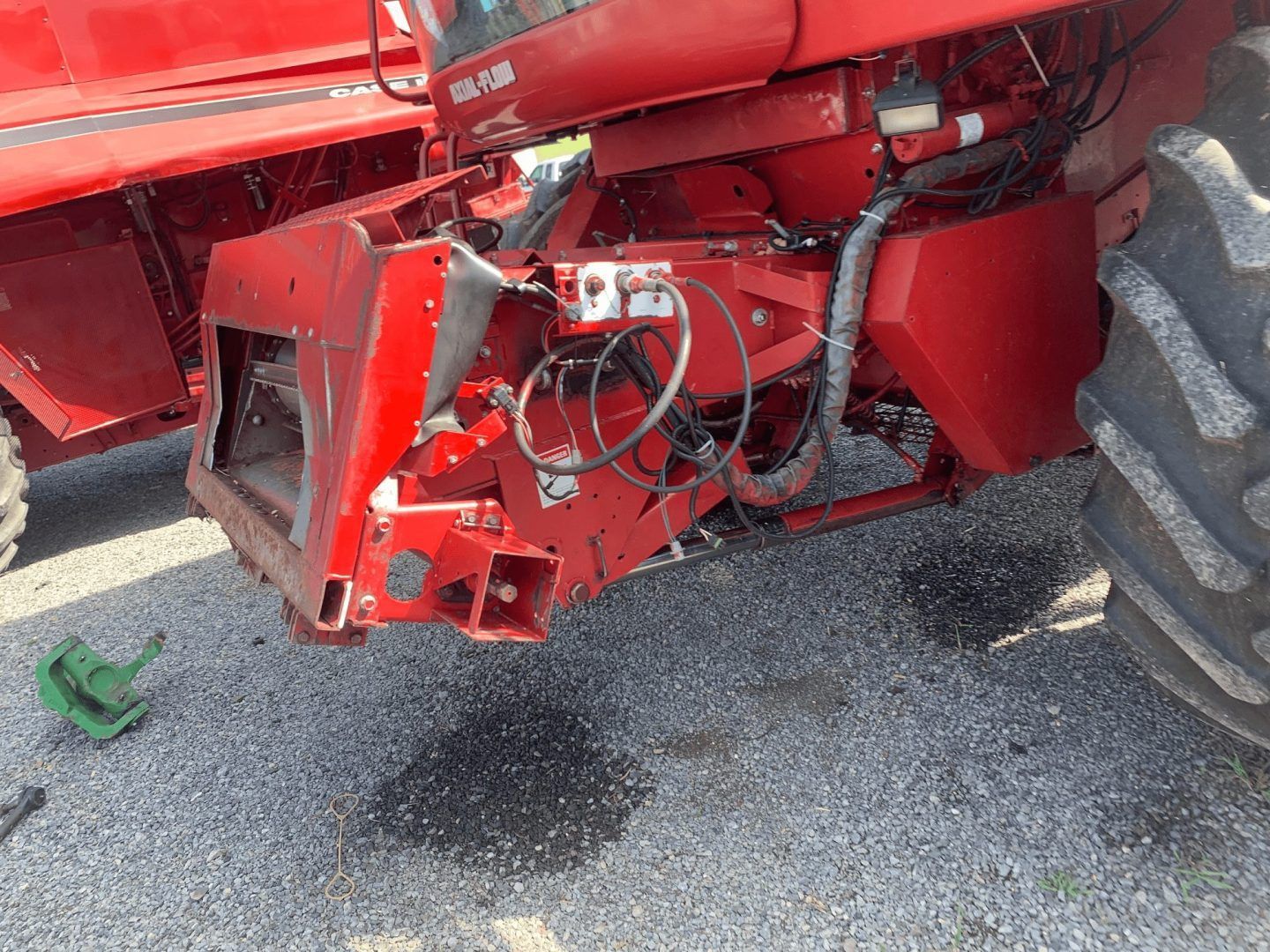 Close-up of red farm machinery with hoses and a large tire on gravel.