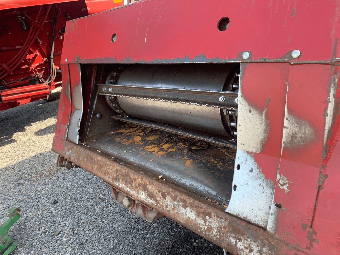 Close-up of a red agricultural machine with a visible metal roller and worn, dirty lower panel