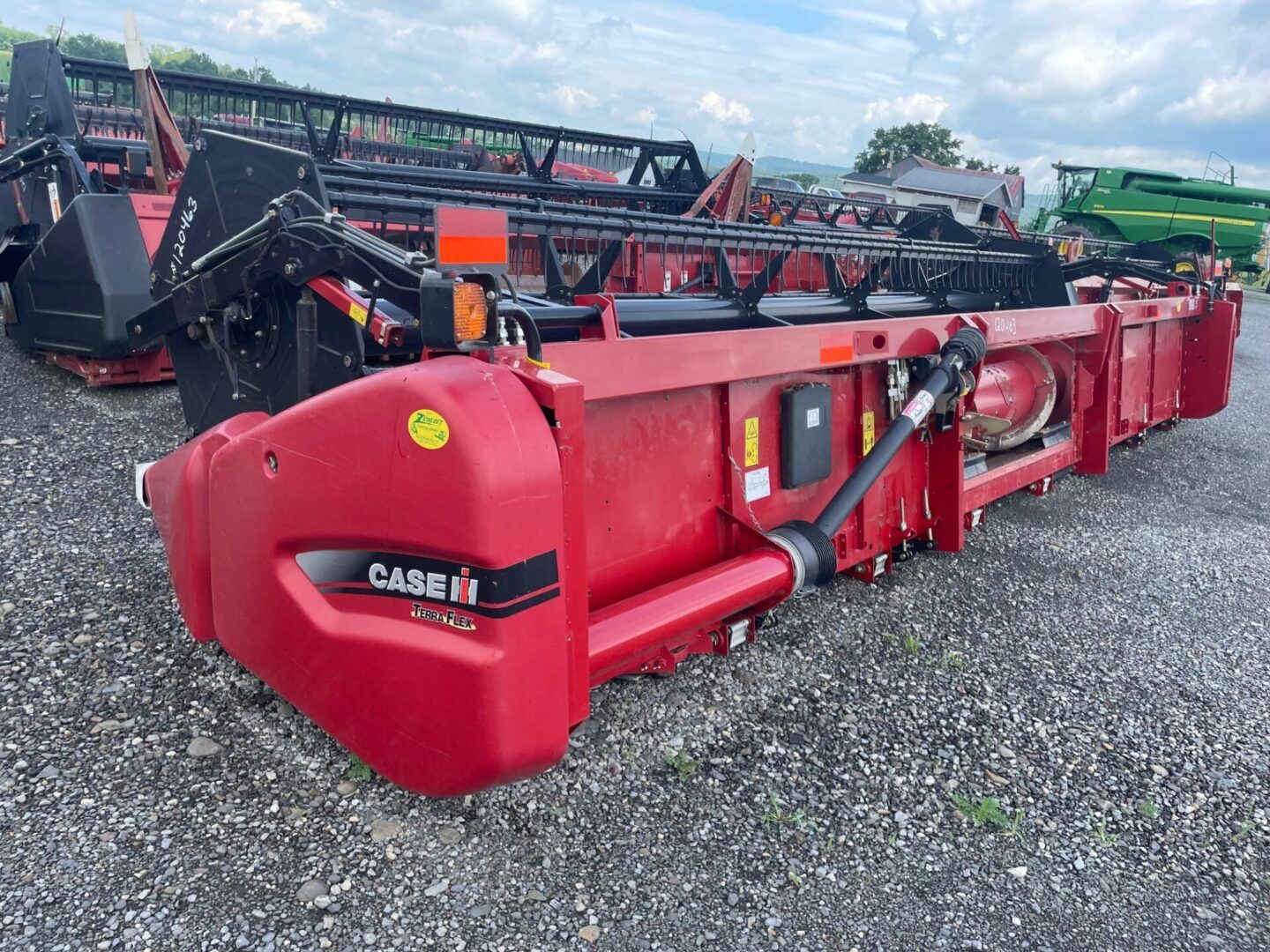 Red Case IH combine header on gravel lot with other farm equipment in background