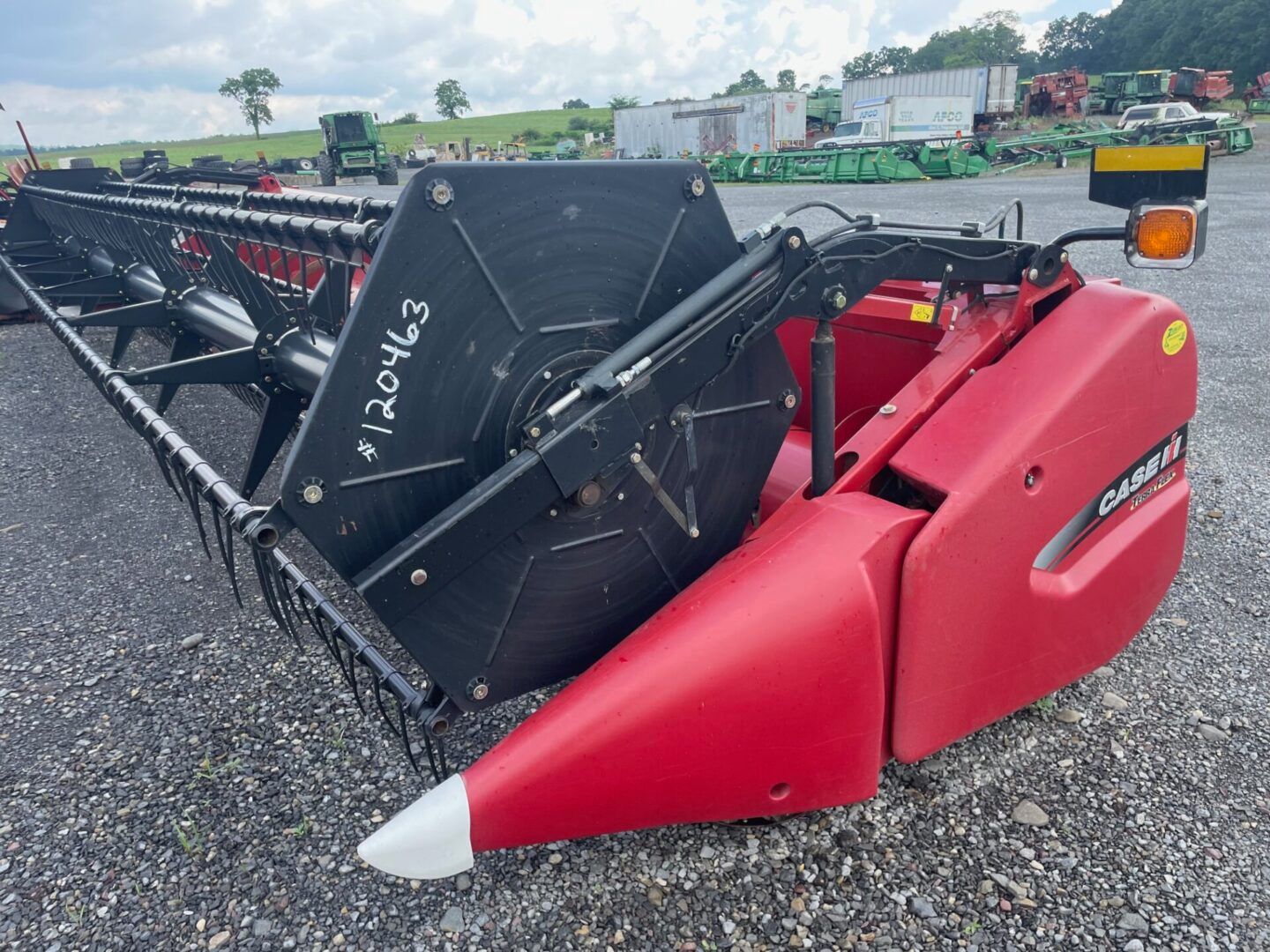 Red and black combine harvester header on gravel lot under cloudy sky