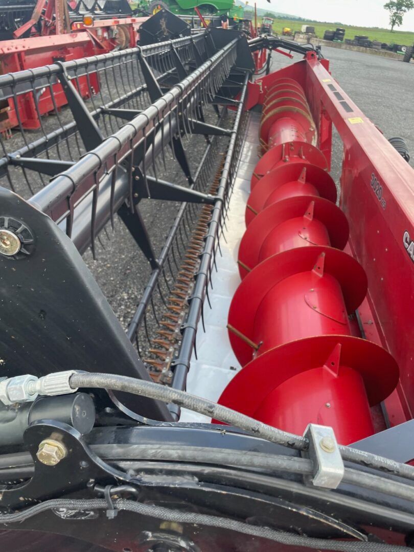 Red spiral auger inside a farm harvester, viewed from above along the machine’s metal conveyor.