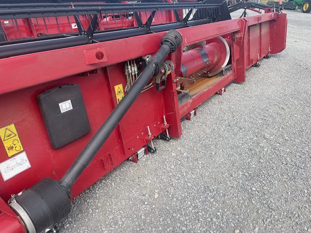 Red farm machine attachment with black hydraulic hoses on gravel