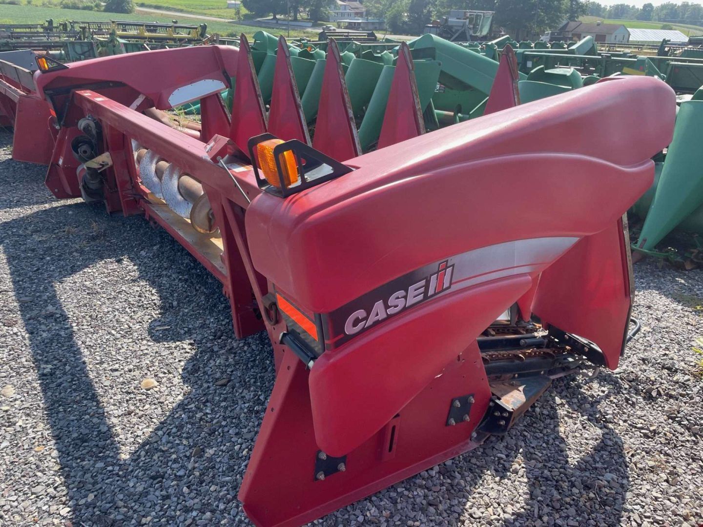 Red CASE IH corn header with green corn snouts displayed outdoors on gravel.