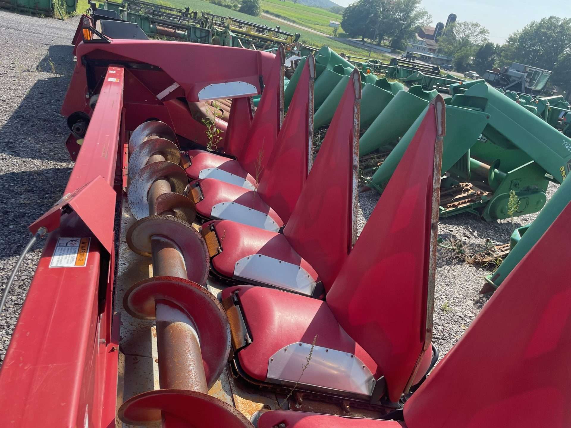 Red combine harvester header with metal intake blades in a field, viewed from above