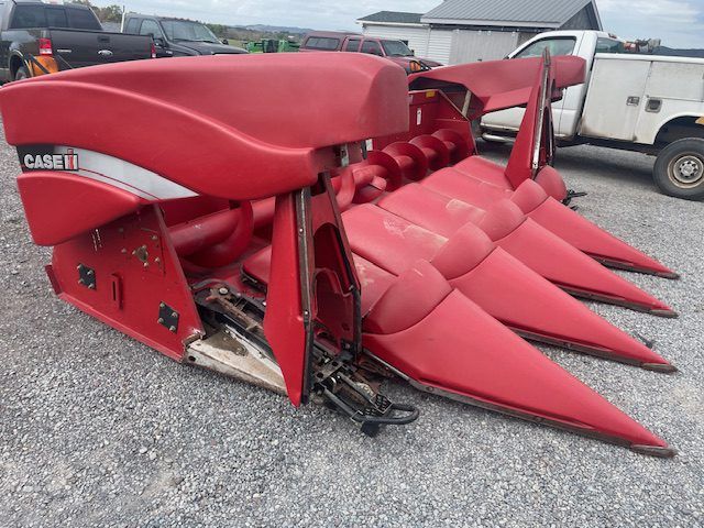 Red Case IH farm implement with pointed prongs parked on gravel lot