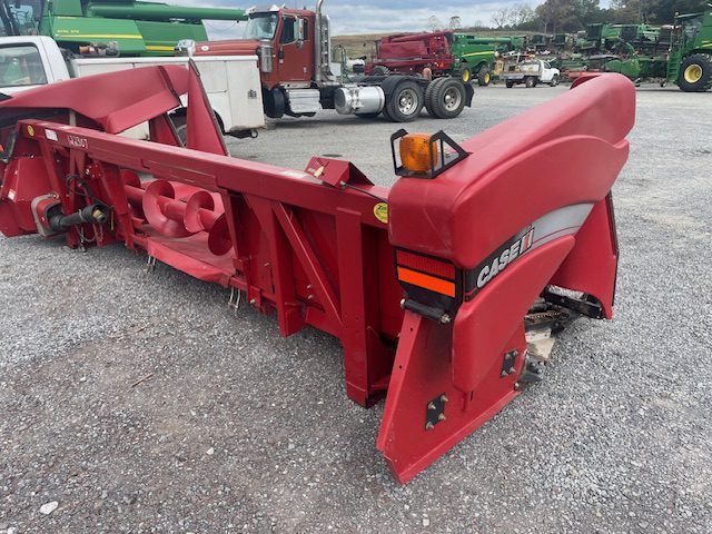 Large red snowplow blade attachment on a gravel lot, with trucks in the background.