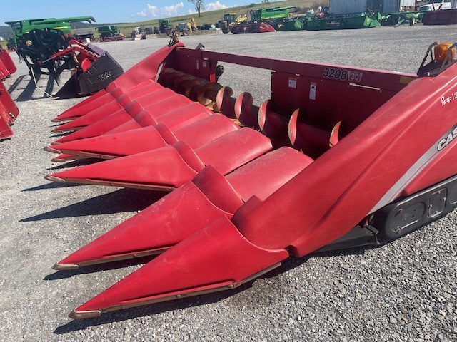 Red agricultural corn header with pointed red cones on a gravel lot at an equipment yard