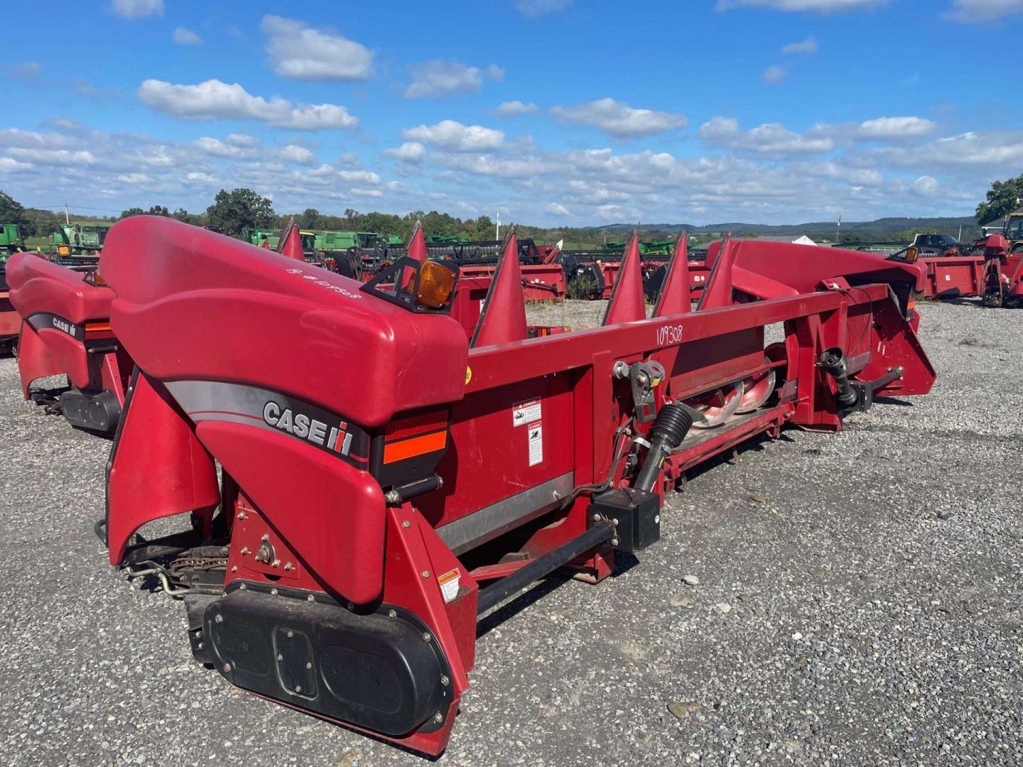 Red Case IH farm implement on gravel lot under a blue sky, with other equipment in the background