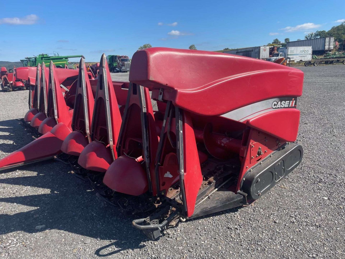 Red agricultural header attachment, bright red, sitting on gravel under a clear blue sky.