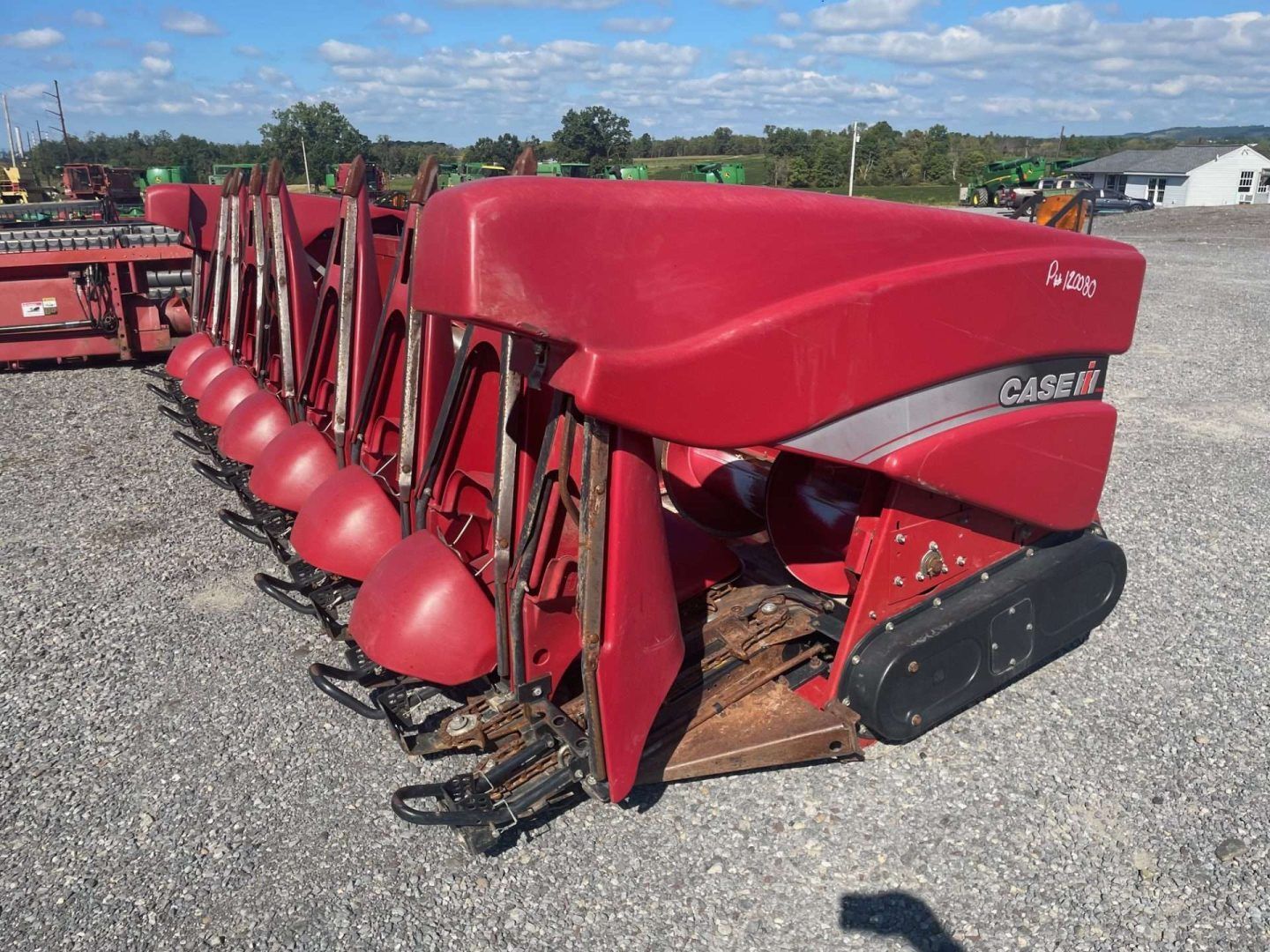 Red agricultural combine header attachment lined up on gravel, with red covers and metal cutting points.
