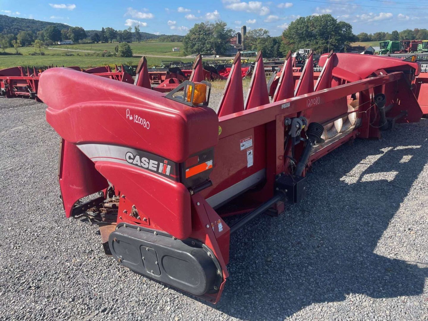 Red CASE IH corn header on a gravel lot, with rows of pointed red harvesting cones.