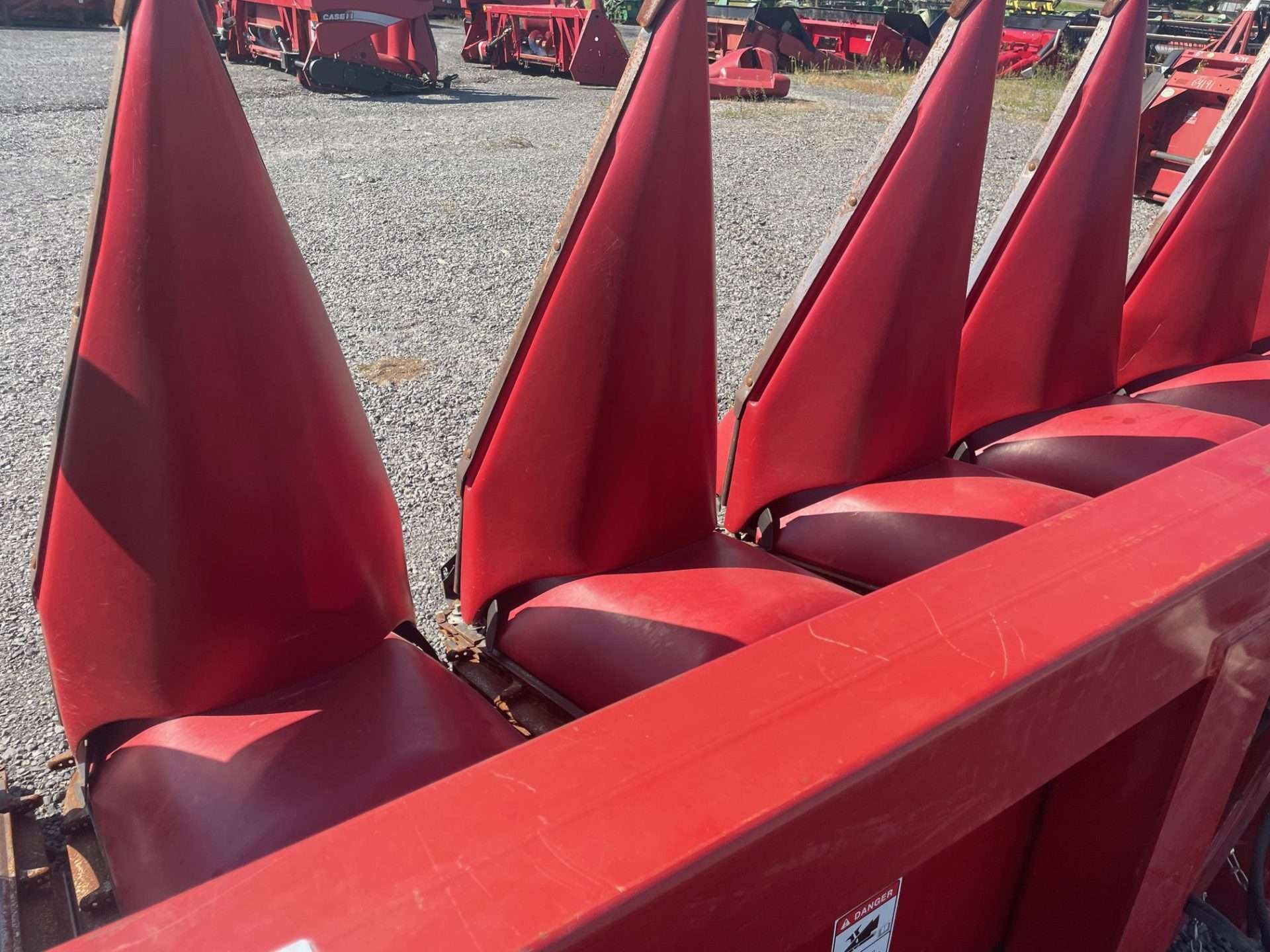 Row of red cone-shaped chairs on a gravel lot, with a red bench in the foreground.