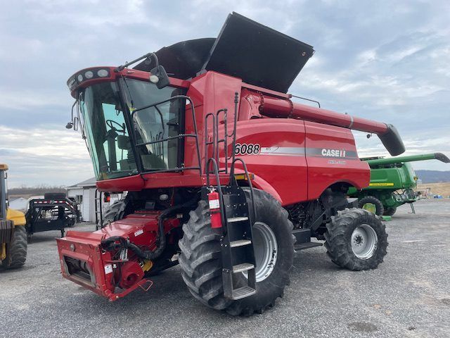 Red combine harvester with raised grain tank in a farm lot under cloudy sky