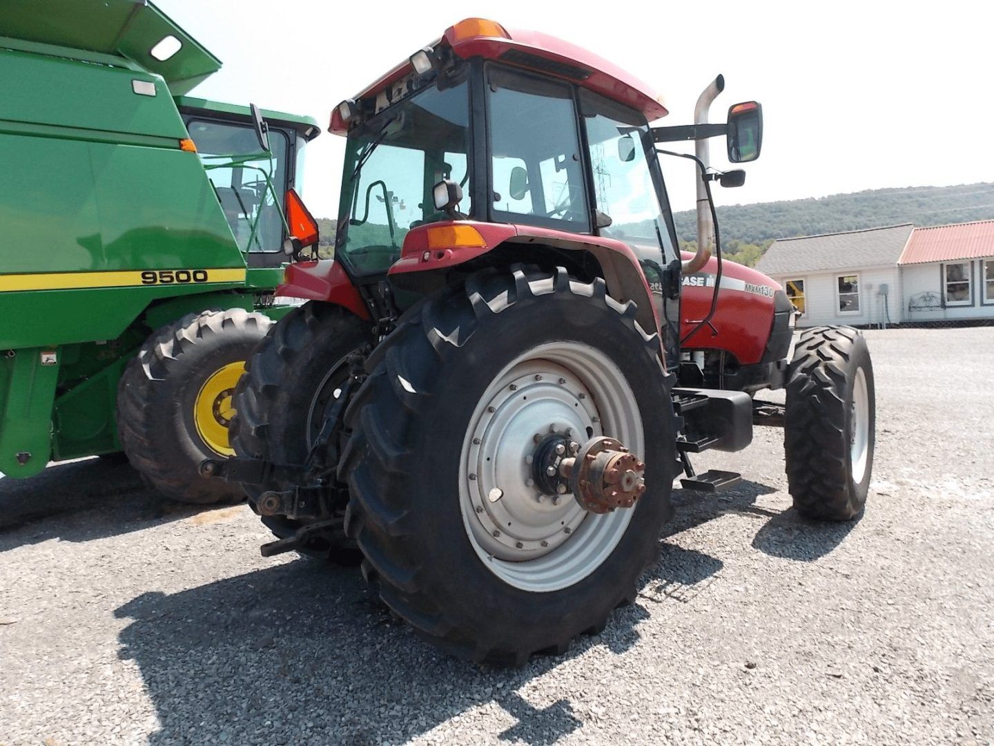 Red tractor with large rear tires parked on gravel beside a green farm machine.