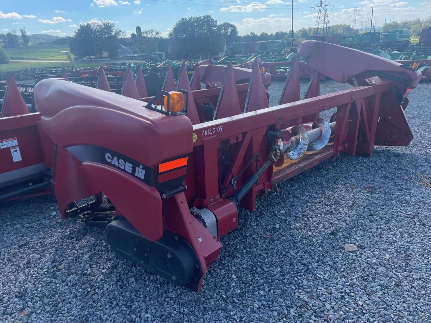 Red agricultural combine header on gravel lot under cloudy sky