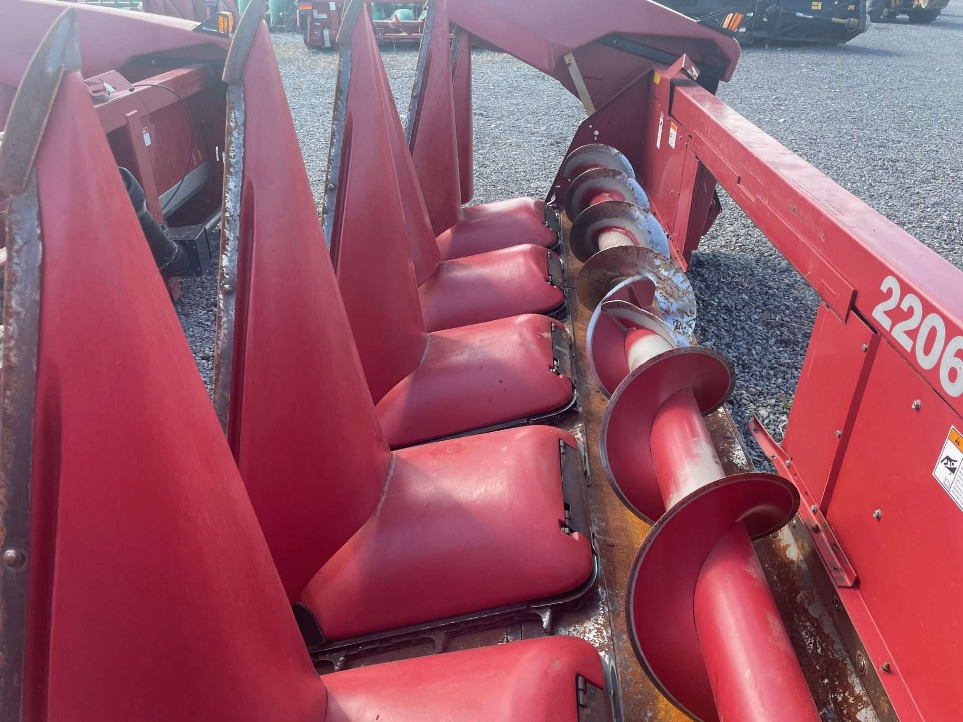 Red farm harvester header with rotating auger and red metal tines close-up