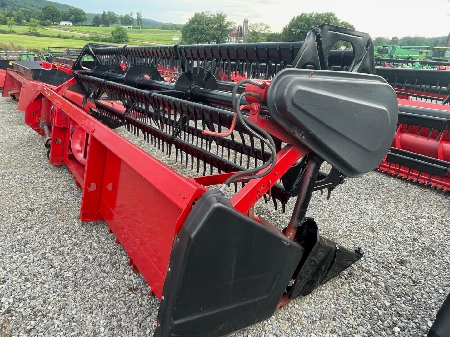Red combine harvester header with black reel, parked on gravel in a field
