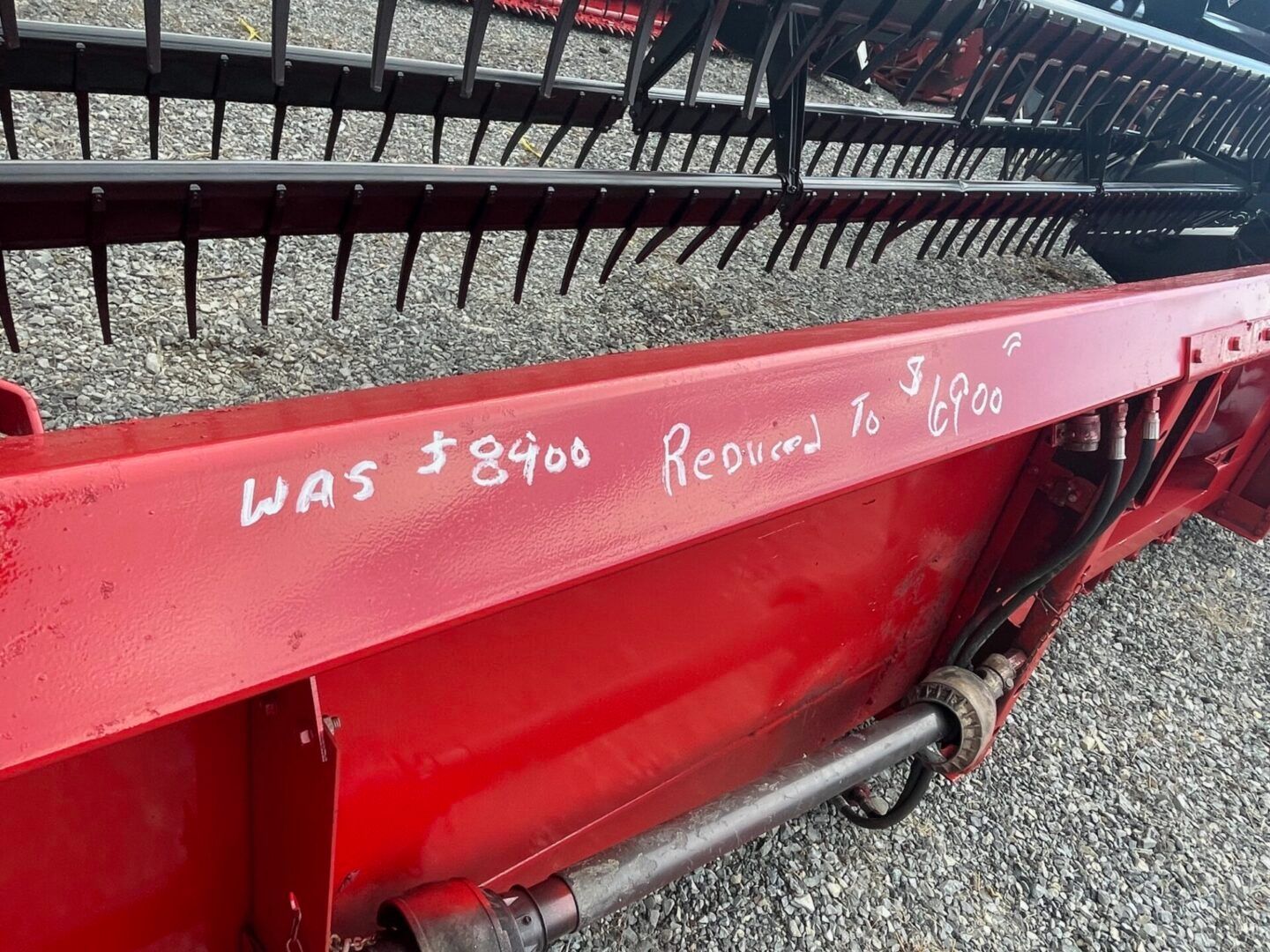 Red farm machine with handwritten white text and a black mesh conveyor behind it