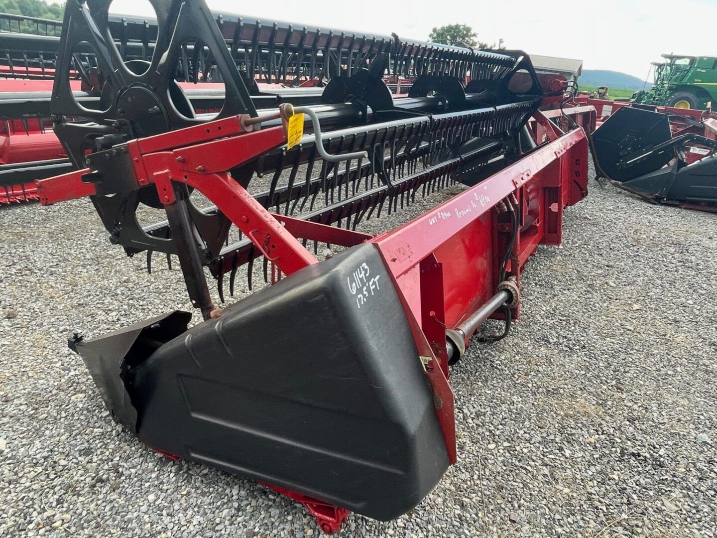 Red agricultural combine header with black reel and triangular end guard on gravel lot