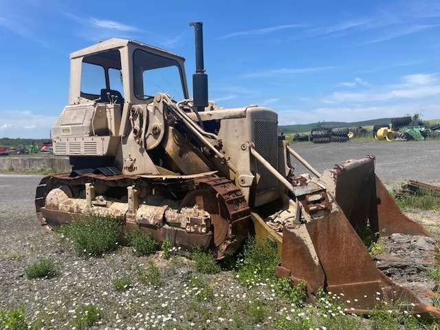 Old beige bulldozer with rusted blade in a gravel lot under a blue sky