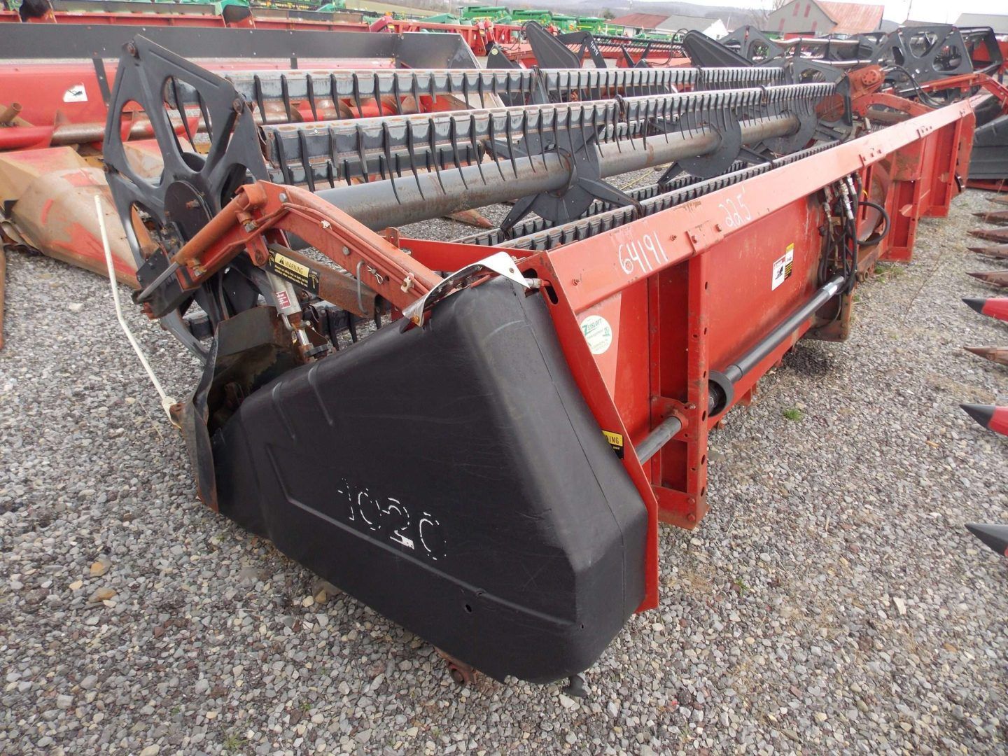 Red agricultural combine header with black reel and red frame on gravel lot
